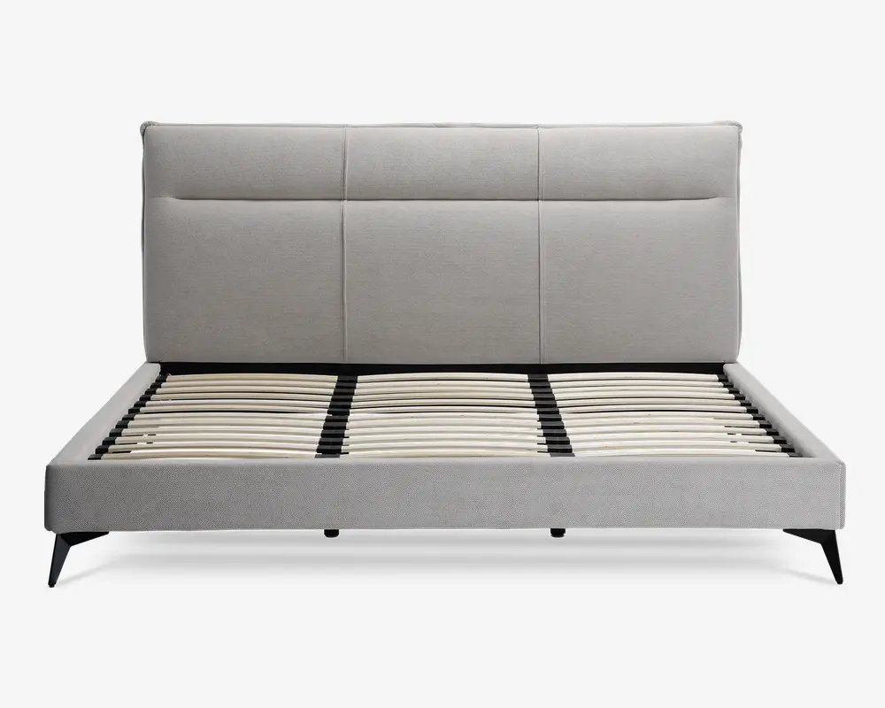 Moderne sengegavl med en høj, rektangulær polstret hovedgavl i lysegråt stof, med diskrete lodrette og vandrette syninger, der giver et paneludseende. Rammen har rene linjer og er også polstret i matchende lysegråt stof. Bunden har jævnt fordelte lameller af træ til støtte for madrassen, og sengen står på skråtstillede sorte ben for et moderne udtryk.