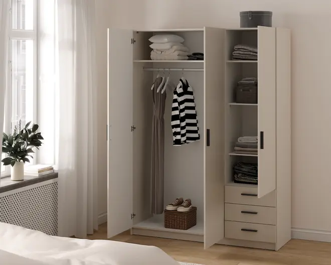 Et beige garderobeskab med tre låger, der har en kombination af bøjlestang, hylder og skuffer. Venstre og midterste sektion har en bøjlestang med tøj på bøjler, og øverste hylde rummer sammenfoldet sengetøj og håndklæder. Højre sektion har flere hylder med pænt sammenfoldet tøj, opbevaringskurve og tre udtræksskuffer nederst. Skabet har enkle sorte greb og et moderne, minimalistisk design.