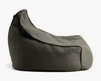 Et sidebillede af et blødt, formfast sæde med høj rygstøtte og skrånende siddeflade. Stoffet ser ud til at være et tekstureret, tæt vævet materiale i en neutral grå farve. Syningerne er synlige og giver sædet en markeret form og ekstra holdbarhed. Designet er afslappet og komfortabelt, velegnet til afslapning.