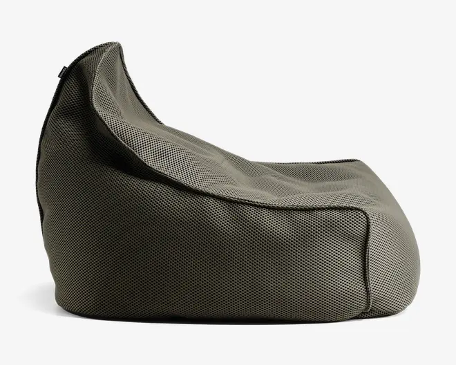 Et sidebillede af et blødt, formfast sæde med høj rygstøtte og skrånende siddeflade. Stoffet ser ud til at være et tekstureret, tæt vævet materiale i en neutral grå farve. Syningerne er synlige og giver sædet en markeret form og ekstra holdbarhed. Designet er afslappet og komfortabelt, velegnet til afslapning.