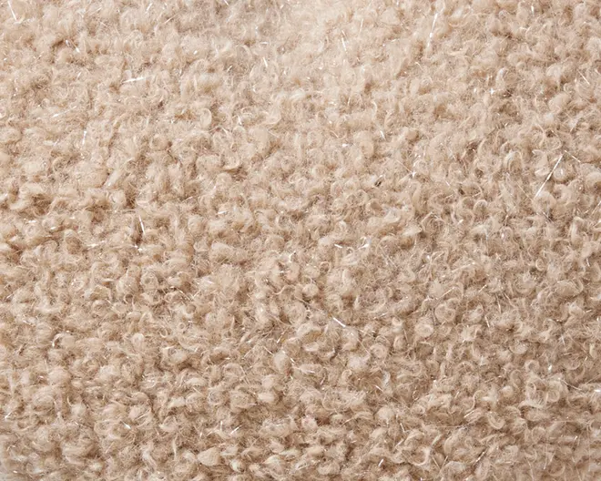Nærbillede af et tekstureret, beige bouclé-stof med tætte, løkkede garner, der giver en blød og hyggelig overflade. Materialet har et let ujævnt, nopret udseende med diskrete farvevariationer og små, skinnende fibre spredt ud over for ekstra visuel effekt.