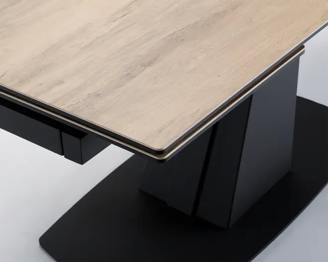 Nærbillede af et bordhjørne med en lys træbordplade med glat, mat finish. Bordpladen har en skrå kant og hviler på en solid, moderne sort base med geometriske linjer og en bred, flad bund for stabilitet.