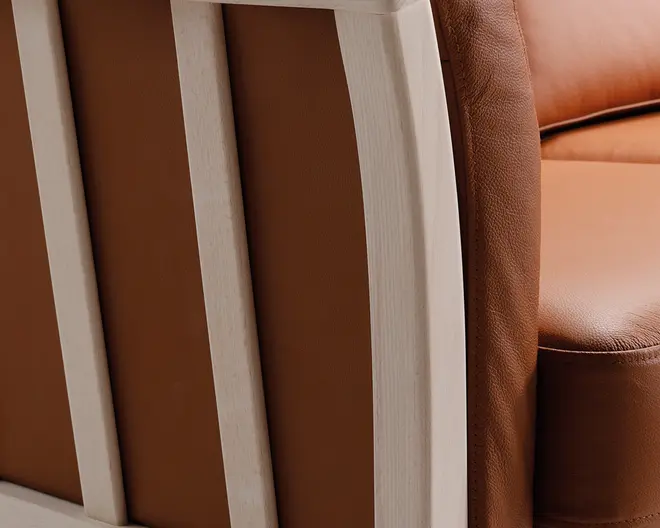 Nærbillede af et møbel med glat, lysebrunt læderbetræk og en ramme af lyst træ. Læderet ser blødt og velpolstret ud med synlige syninger langs kanterne. Trærammen har en naturl sopret conc og lodrette lameller, hvilket giver møblet et moderne og elegant udtryk,.