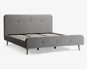 En moderne sengeramme med et lysegråt polstret hovedgærde og fodgærde, begge med enkle knapdetaljer. Rammen har rene, afrundede kanter og står på fire lyse træben. Bundrammen består af jævnt fordelte lameller i træ til støtte for madrassen. Designet er minimalistisk og nutidigt.