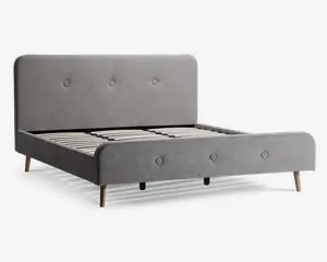 En moderne sengeramme med et lysegråt polstret hovedgærde og fodgærde, begge med enkle knapdetaljer. Rammen har rene, afrundede kanter og står på fire lyse træben. Bundrammen består af jævnt fordelte lameller i træ til støtte for madrassen. Designet er minimalistisk og nutidigt.