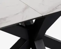 Nærbillede af et bordhjørne med en hvid bordplade i marmorlook med diskrete grå årer og en skrå kant. Bordpladen understøttes af en solid, sort metalbase i krydsform, hvilket giver bordet et moderne og elegant udtryk.
