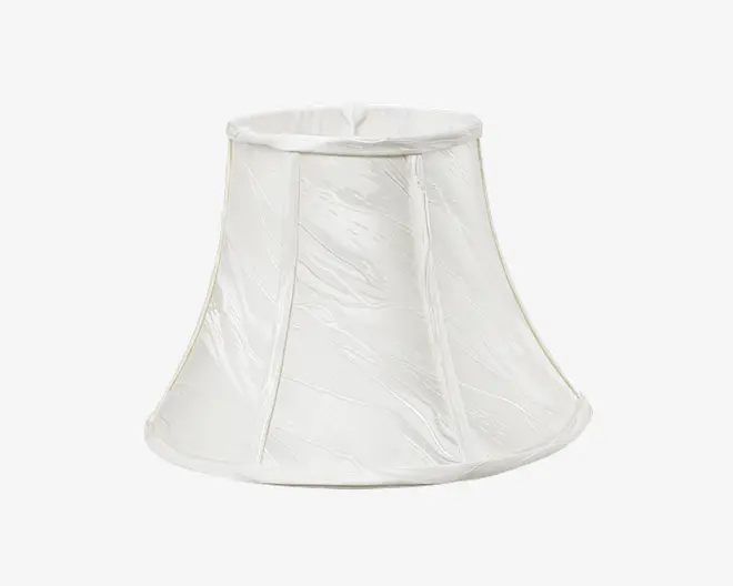 En klokkeformet lampeskærm lavet af hvidt stof med et diskret tekstureret mønster. Skærmen har lodrette syninger, der deler den i paneler, og en let udvidet bundkant. Top- og bundkanterne er afsluttet med en glat stofkant.