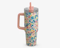 Høj, isoleret drikkebæger med stort lyserødt håndtag og gennemsigtigt låg med lyserødt sugerør. Ydersiden er dekoreret med et farverigt blomsterdesign med blå, gule og lyserøde blomster samt grønne blade på en lyserød baggrund.