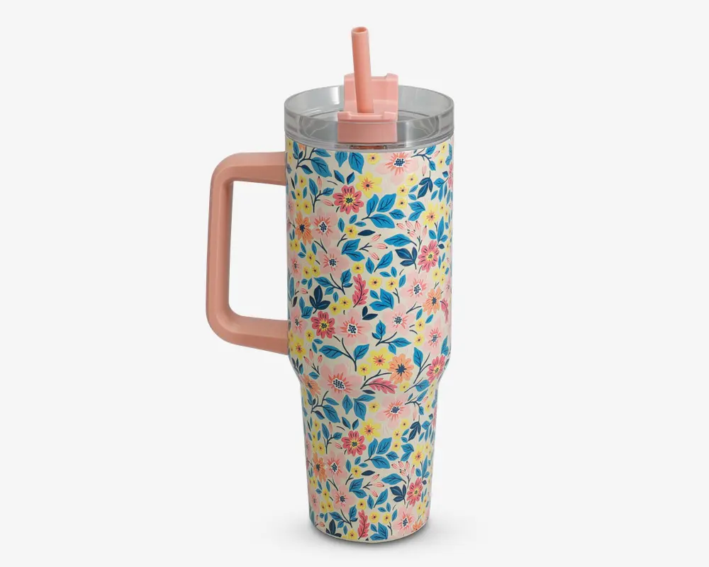Høj, isoleret drikkebæger med stort lyserødt håndtag og gennemsigtigt låg med lyserødt sugerør. Ydersiden er dekoreret med et farverigt blomsterdesign med blå, gule og lyserøde blomster samt grønne blade på en lyserød baggrund.