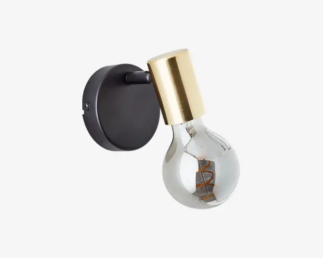 Væghængt lampe med en rund sort metalbase og en cylindrisk fatning i messing. Lampen har en klar, rund pære med synlig glødetråd, hvilket giver et moderne og industrielt udtryk. Kombinationen af messing og sort tilføjer elegance og kontrast.