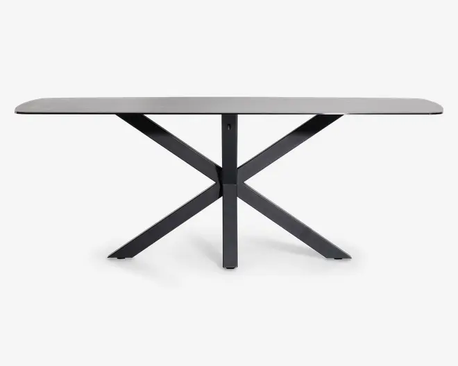 Rektangulært bord med en glat, lys bordplade og et moderne, sort metalstel med fire skrå ben, der krydser hinanden i midten for et stabilt og geometrisk udtryk.