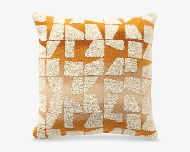 Firkantet pyntepude med et struktureret creme- og orange geometrisk mønster, med uregelmæssige blokformer og en blød, luvet vævet overflade.