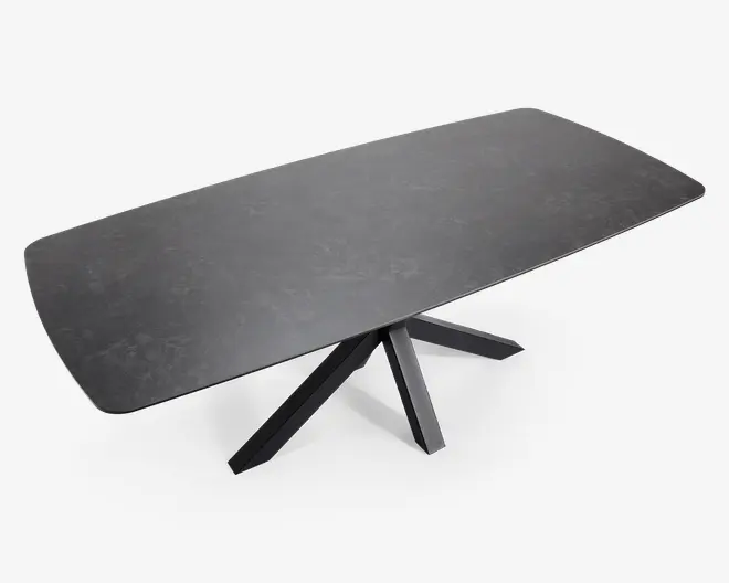 Rektangulært bord med en mat sort overflade og diskrete marmoreringer. Bordpladen har blødt afrundede hjørner og kanter. Bordet understøttes af en moderne, geometrisk sort metalbase med fire skrå ben, der mødes i midten og giver et stabilt og stilfuldt udtryk.