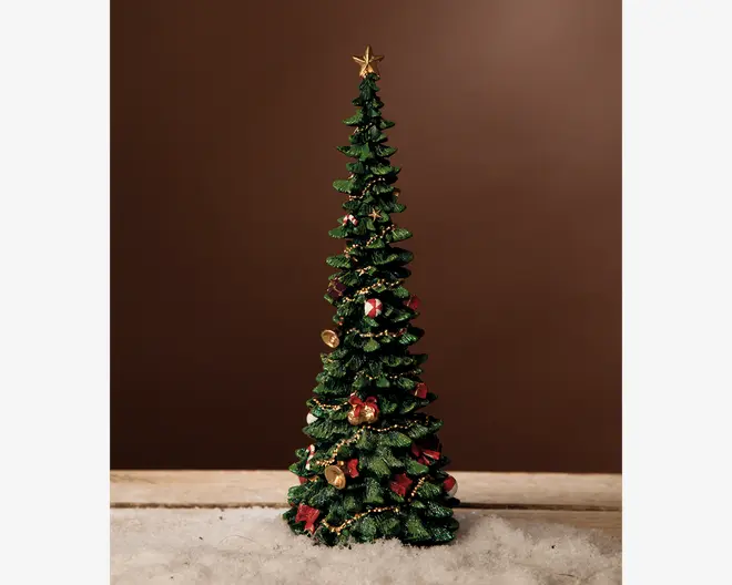 Høj, slank kunstig juletræ med tætte grønne grene. Pyntet med guldfarvet guirlande, røde sløjfer, små guldfarvede ornamenter og miniatureindpakkede gaver. Toppen af træet har en guldfarvet stjerne. Træet står på en overflade dækket af kunstig sne, hvilket giver et festligt udtryk.