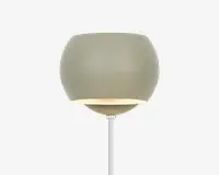 Moderne væglampe med en glat, mat lysegrå overflade. Lampen har en rund, skålformet skærm med en let åben bund, der lader lyset skinne nedad. Designet er minimalistisk og nutidigt, med en slank stang, der forbinder skærmen til vægbeslaget.