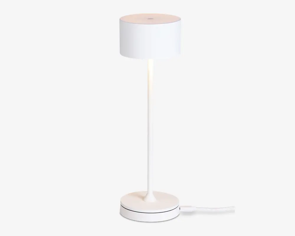 En moderne, minimalistisk lampe med en cylindrisk hvid lampeskærm, en slank lige stang og en rund fod. Lampen har et rent, helt hvidt udseende og en synlig ledning, der går ud fra bunden. Designet er stilrent og enkelt, velegnet til moderne indretning.