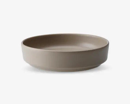En rund, lav skål med en glat, mat overflade i en neutral beige farve. Skålen har lige, lidt tykke sider og en flad bund, hvilket giver et moderne og minimalistisk udtryk. Der er ingen synlige mønstre, teksturer eller dekorationer.