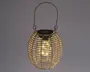 Rund lanterne med et ydre i flettet rattan-look og et metalhåndtag til ophængning. Lanternen har en varm hvid LED-pære indeni, som er synlig gennem det åbne flet, og der er et solcellepanel på toppen til opladning. Designet giver et hyggeligt, stemningsfuldt lys, der egner sig til både udendørs og indendørs brug.