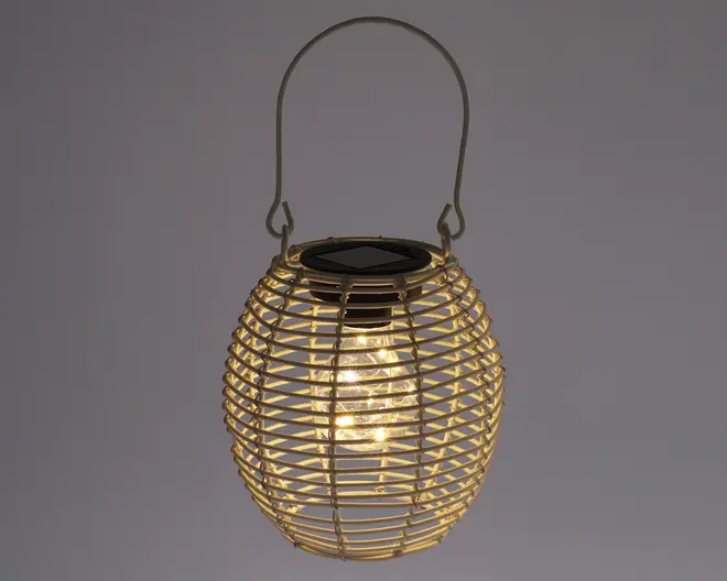 Rund lanterne med et ydre i flettet rattan-look og et metalhåndtag til ophængning. Lanternen har en varm hvid LED-pære indeni, som er synlig gennem det åbne flet, og der er et solcellepanel på toppen til opladning. Designet giver et hyggeligt, stemningsfuldt lys, der egner sig til både udendørs og indendørs brug.