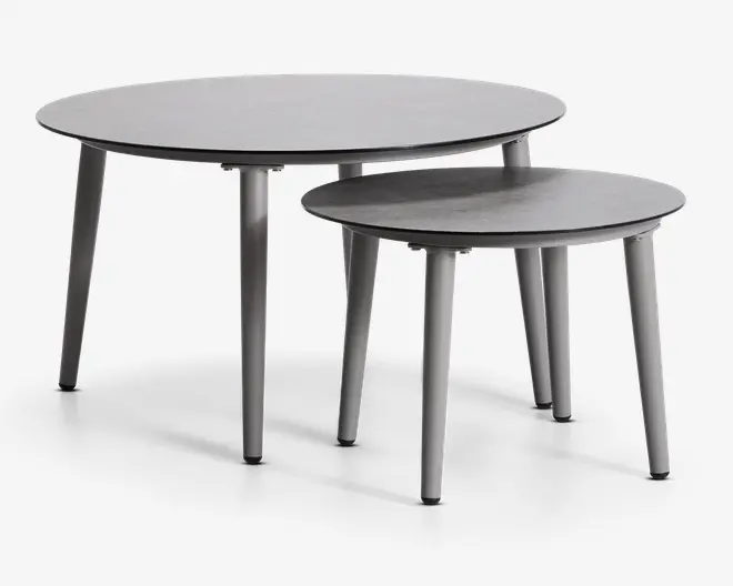 Sæt med to indskudsborde i et moderne, minimalistisk design. Begge borde har runde, glatte bordplader med mat grå finish og let tilspidsede ben. Det mindre bord kan skubbes delvist ind under det større for pladsbesparende opbevaring. De rene linjer og neutrale farve gør dem alsidige til forskellige indretninger.