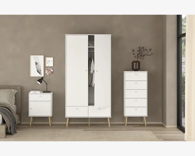 Billedet viser et sæt moderne soveværelsesmøbler med et minimalistisk design. Møblerne er hvide med lyse træben og små runde greb. Sættet består af et højt garderobeskab med to låger, hvor den ene er let åben og afslører hængende tøj og en hylde, samt to skuffer nederst. Ved siden af garderobeskabet står en kommode med fem rummelige skuffer, og på den anden side er et natbord med en enkelt skuffe og en åben hylde nedenunder. Natbordet er dekoreret med en sort skrivebordslampe og stakke af bøger, mens kommoden har en brun vase med dekorative grene. Møblerne står op ad en taupefarvet væg, og rummet har lyst trægulv og et stort vindue, der lukker naturligt lys ind.