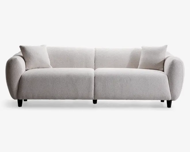 Moderne sofa med minimalistisk design og blødt, tekstureret lysebeige betræk. Sofaen har brede, afrundede armlæn og lav ryg, hvilket giver et hyggeligt og indbydende udtryk. Der medfølger to matchende, firkantede puder, én i hver ende. Sæde- og ryghynderne er tykke og bløde for ekstra komfort. Sofaen står på korte, næsten usynlige ben, hvilket giver et svævende udseende.