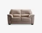 En to-personers sofa med blødt, lysebeige stofbetræk. Sofaen har fyldige, polstrede ryghynder og brede, polstrede armlæn for ekstra komfort. Sædehynderne er tykke og let buede foran, hvilket giver ergonomisk støtte. Sofaen står på korte, solide sorte ben.