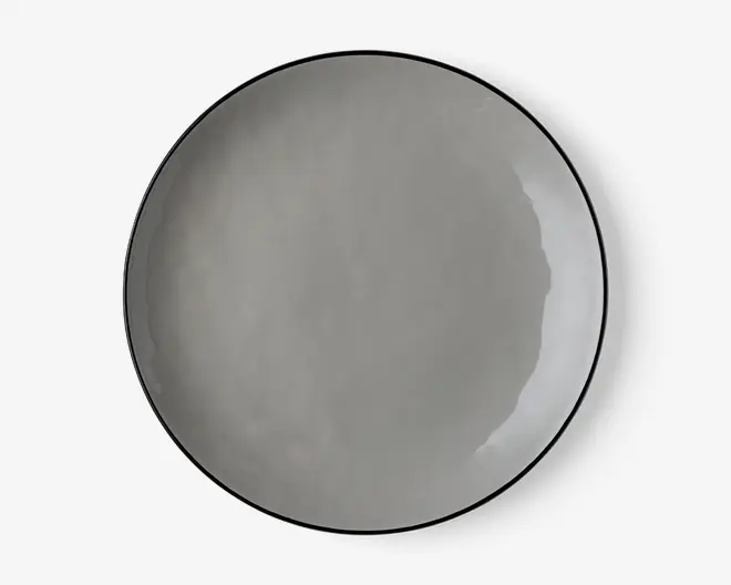 En rund, flad tallerken med en glat, blank overflade i en ensfarvet grå nuance. Tallerkenen har et minimalistisk design med en let hævet kant og et diskret, moderne udtryk. Kanterne er tynde, og finishen er jævn, hvilket giver et stilrent og nutidigt udseende.