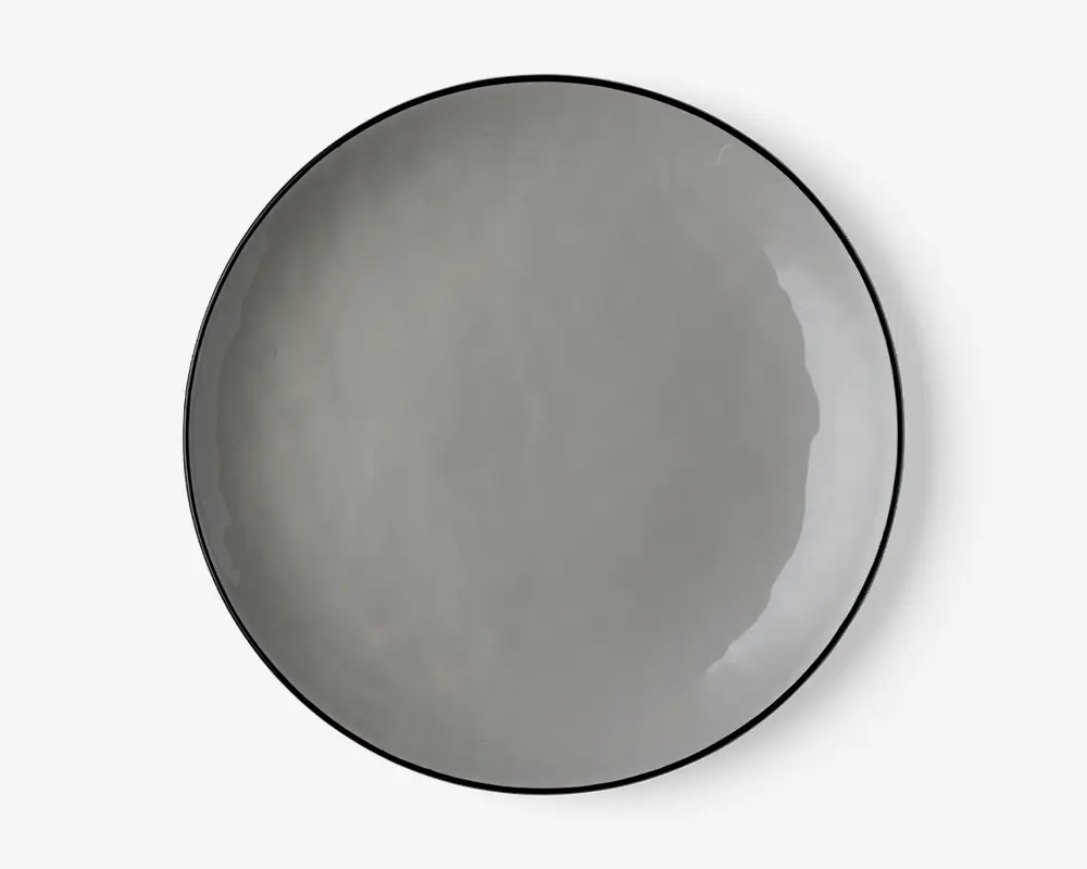 En rund, flad tallerken med en glat, blank overflade i en ensfarvet grå nuance. Tallerkenen har et minimalistisk design med en let hævet kant og et diskret, moderne udtryk. Kanterne er tynde, og finishen er jævn, hvilket giver et stilrent og nutidigt udseende.