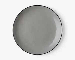 En rund, flad tallerken med en glat, blank overflade i en ensfarvet grå nuance. Tallerkenen har et minimalistisk design med en let hævet kant og et diskret, moderne udtryk. Kanterne er tynde, og finishen er jævn, hvilket giver et stilrent og nutidigt udseende.