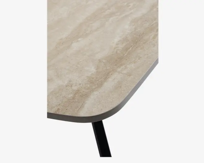 Nærbillede af en bordplade med en lys beige, stenlignende overflade med diskrete naturlige årer. Kanten er let afrundet, og bordpladen understøttes af et sort metalben.