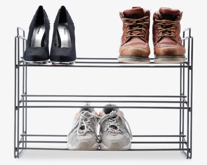 Trestykket metalstativ med et minimalistisk, åbent design. Stativet er sølvfarvet og lavet af tynde, rørformede metalstænger. Hver hylde består af parallelle stænger, der giver støtte til forskellige typer fodtøj. Stativet er vist med et par sorte højhælede sko, brune læderstøvler og hvide sportssko, hvilket demonstrerer dets kapacitet og alsidighed til forskellige skotyper.