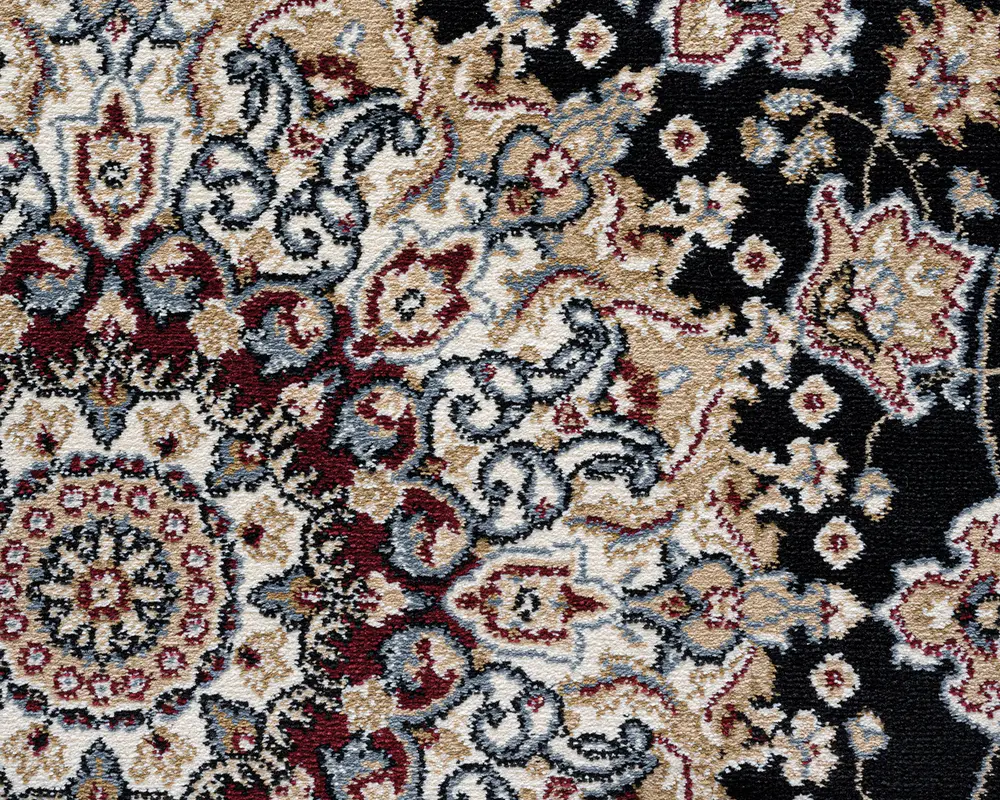 Nærbillede af et traditionelt vævet tekstil med et indviklet blomster- og medaljonmønster. Designet har en blanding af creme, bordeaux, sort og blågrå farver med udsmykkede, snoede motiver og detaljerede kanter. Teksturen ser blød og tæt ud, hvilket tyder på en fyldig luv. Mønstret er symmetrisk og rigt detaljeret, hvilket giver et klassisk og elegant udtryk.