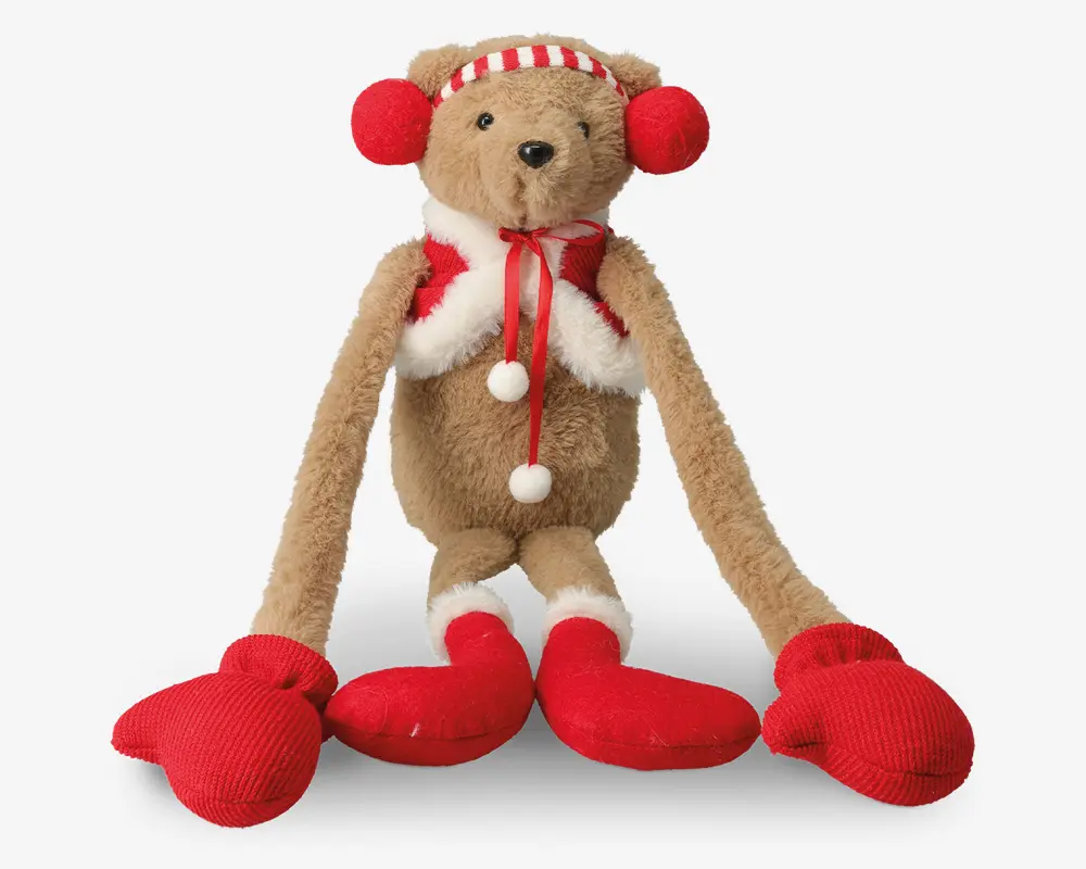 Bamse med lange arme og ben, iført røde vanter, røde støvler, rød- og hvidstribet hue samt røde ørevarmere. Bamsen har også et hvidt og rødt tørklæde med blødt hvidt kant og pomponer. Pelsen er lysebrun, og næsen er sort.
