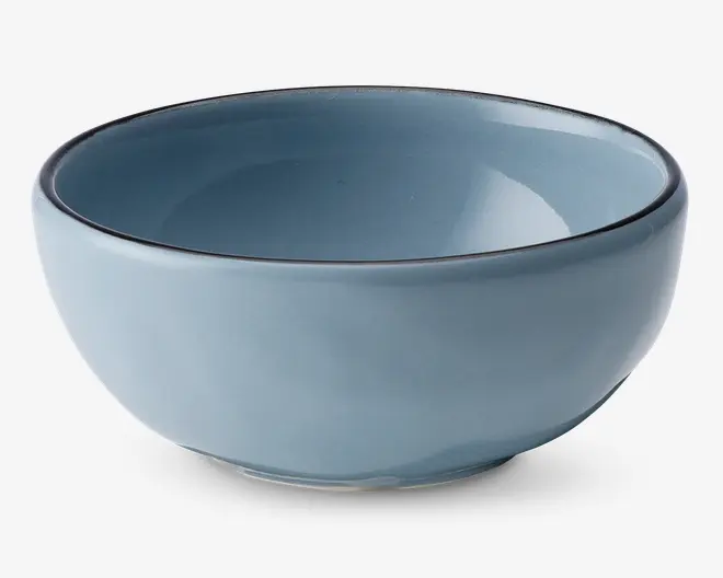 En rund, mellemstor skål af keramik med en glat, blank lyseblå overflade. Skålen har en let tyk kant med en diskret mørk kant og en blødt buet form, der smalner ind mod en lille, stabil fod. Både indersiden og ydersiden har samme farve, hvilket giver et moderne og minimalistisk udtryk.