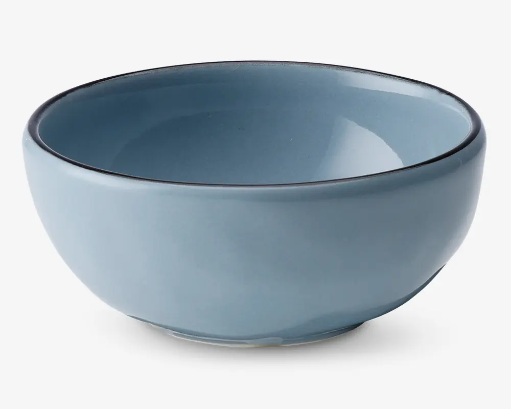 En rund, mellemstor skål af keramik med en glat, blank lyseblå overflade. Skålen har en let tyk kant med en diskret mørk kant og en blødt buet form, der smalner ind mod en lille, stabil fod. Både indersiden og ydersiden har samme farve, hvilket giver et moderne og minimalistisk udtryk.