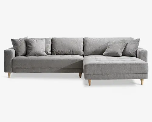 Moderne L-formet sofa med lysegråt stofbetræk, rene linjer og et minimalistisk design. Sofaen har fem løse ryghynder og to matchende pyntepuder for ekstra komfort. Sædehynderne er let knapstukne for et diskret dekorativt udtryk. Sofaen står på korte, skrå træben i naturfarve, som giver stabilitet og et moderne udtryk. Chaiselong-delen er placeret til højre, når man ser på sofaen forfra.