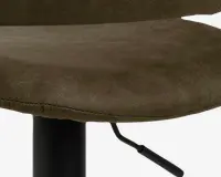 Nærbillede af et sæde med olivengrønt betræk, der ligner ruskind, og synlige syninger langs kanten. Sædet er let buet for komfort og er monteret på en sort metalbase med et håndtag til højdejustering.