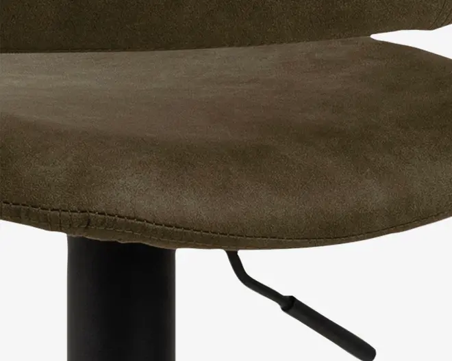 Nærbillede af et sæde med olivengrønt betræk, der ligner ruskind, og synlige syninger langs kanten. Sædet er let buet for komfort og er monteret på en sort metalbase med et håndtag til højdejustering.