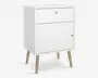 Et kompakt, moderne skab med mat hvid finish, der har en øverste skuffe og et nederste skabsrum med låge. Både skuffen og lågen har små, runde knopper i lyst træ. Skabet står på fire skråtstillede ben i lyst træ, hvilket giver det et udtryk i retro stil.