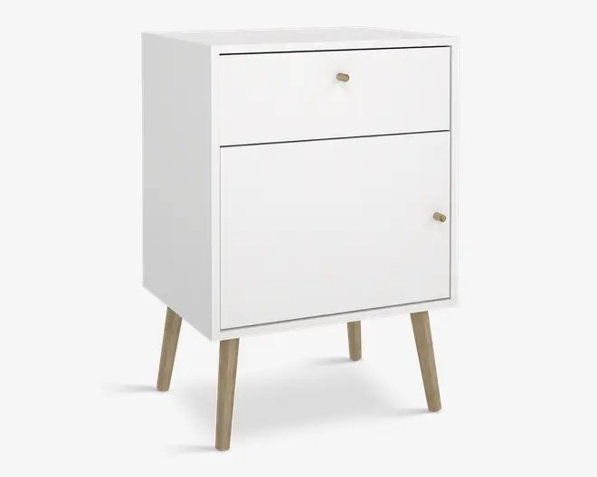 Et kompakt, moderne skab med mat hvid finish, der har en øverste skuffe og et nederste skabsrum med låge. Både skuffen og lågen har små, runde knopper i lyst træ. Skabet står på fire skråtstillede ben i lyst træ, hvilket giver det et udtryk i retro stil.