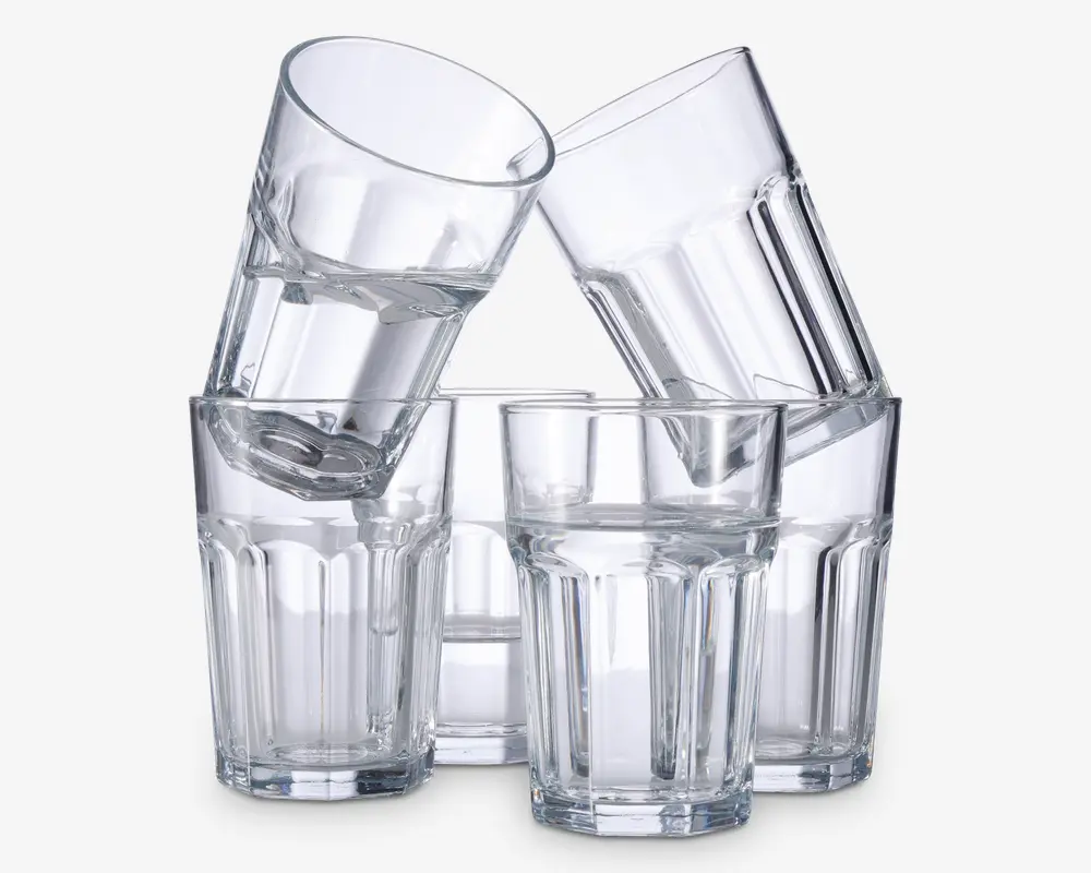 Sæt med seks klare glas med facetslebet design og tykke, solide bunde. Glassene har en let konisk form og lodrette riller langs siderne, hvilket giver et godt greb. To af glassene er stablet skråt ned i de andre, hvilket viser, at de er stabelbare og nemme at opbevare.