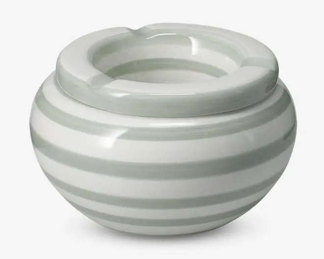 Rund keramisk beholder med bred, tyk kant, der har tre riller til at hvile genstande. Overfladen er dekoreret med vandrette lysegrå og hvide striber, hvilket giver et moderne og rent udtryk. Den blanke finish tilføjer et elegant præg.