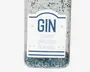 Et nærbillede af en gennemsigtig flaske dekoreret med sølv- og blå glimmer. Flasken har en hvid etiket med blå tekst, hvor der står 'GIN' og mindre tekst nedenunder, der siger 'TO MAKE CHRISTMAS BEARABLE.' Etiketten er pyntet med små stjerner og blå linjer for et festligt udtryk.