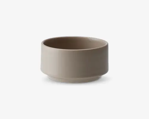 En lille, rund skål med en glat, mat overflade i en lys beige farve. Skålen har lige sider og en let hævet bund, hvilket giver den et moderne og minimalistisk udtryk. Der er ingen synlige mønstre, hanke eller dekorationer.
