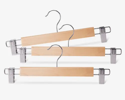 Sæt med tre bøjler i træ med naturfinish, hver med en solid metalkrog og to justerbare metalclips med plastikgreb, der sikrer, at bukser, nederdele eller andre beklædningsgenstande holdes fast uden at glide eller efterlade mærker.