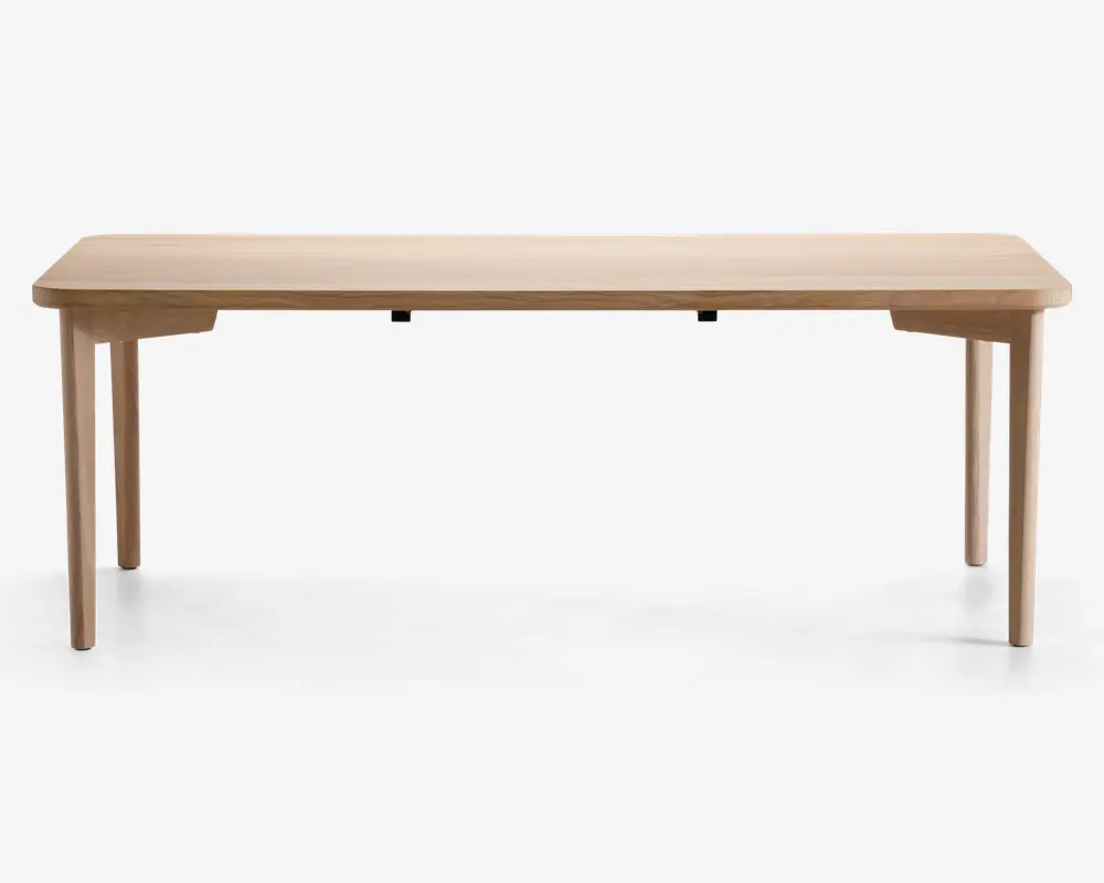 Rektangulært bord med en glat, lys træfinish. Bordet har rene, lige linjer og let afrundede hjørner. Det står på fire solide, let tilspidsede ben, der er placeret yderst i hjørnerne for stabilitet. Designet er minimalistisk og moderne uden synlige beslag eller dekorative elementer.