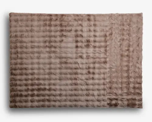 Blød, rektangulær plaid med en plysset, kunstpels-lignende tekstur i en lys taupe farve. Overfladen har et diskret, ternet mønster, som giver et hyggeligt og indbydende udtryk. Kanterne er pænt afsluttede, og materialet fremstår tykt og varmt, perfekt til komfort og varme.