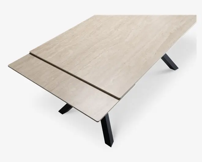 Rektangulært bord med en lys beige bordplade i marmor-look og en synlig udtræksplade i den ene ende. Bordpladen har en glat, blank overflade og understøttes af skrå sorte metalben, hvilket giver et moderne og solidt udtryk.