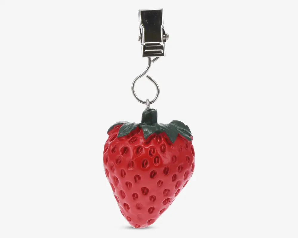 En dekorativ klemme med et realistisk jordbærformet vedhæng. Vedhænget er klart rødt med teksturerede frø og en grøn bladtop, fastgjort til en sølvfarvet metalklemme via en snoet trådsløjfe. Klemmen er robust og designet til sikkert at holde genstande.